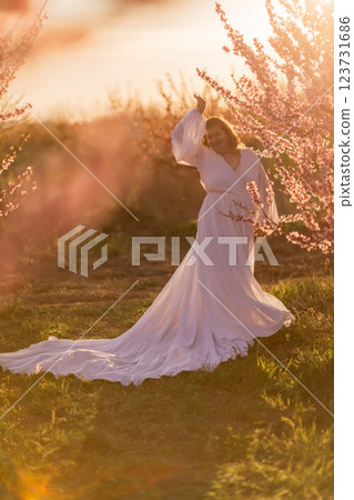 Woman blooming peach orchard. Against the backdrop of a picturesque peach orchard, a woman in a long white dress enjoys a peaceful walk in the park, surrounded by the beauty of nature. Woman blooming peach orchard. Against the backdrop of a picturesque peach orchard, a woman in a long white dress enjoys a peaceful walk in the park, surrounded by the beauty of nature. 123731686
