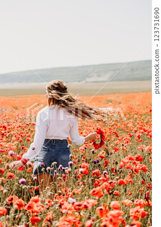Happy woman in a poppy field in a white shirt and denim skirt with a wreath of poppies on her head posing and enjoying the poppy field. Happy woman in a poppy field in a white shirt and denim skirt with a wreath of poppies on her head posing and enjoying the poppy field. 123731690