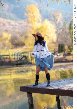 Autumn lake woman. She stands by a pond on a wooden pier in autumn and admires nature. The concept of tourism, weekends outside the city. 123731695