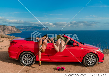 Two women are posing in a red convertible car, one of them is wearing a bikini. Scene is playful and fun. 123731744