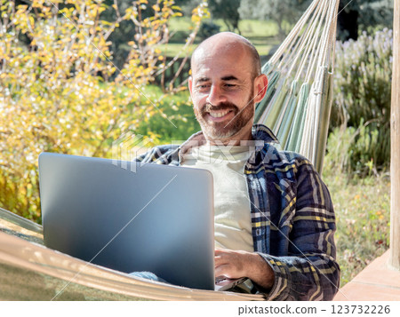 Smiling man working on laptop in hammock Smiling man working on laptop in hammock 123732226