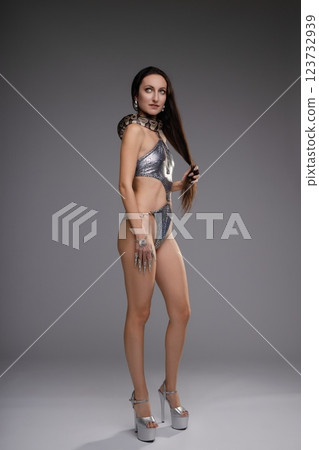 Woman in silver lingerie poses confidently with a snake in a studio setting Woman in silver lingerie poses confidently with a snake in a studio setting 123732939