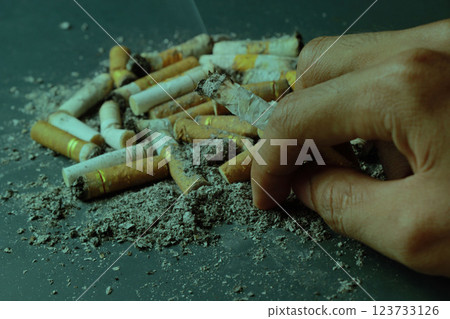 hands holding cigarettes and messy cigarette butts on green gray background hands holding cigarettes and messy cigarette butts on green gray background 123733126