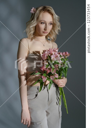 Young woman poses with bouquet of pink flowers in soft lighting indoors Young woman poses with bouquet of pink flowers in soft lighting indoors 123733454