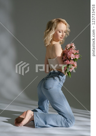 Young woman kneels with flowers wearing light jeans in soft lighting Young woman kneels with flowers wearing light jeans in soft lighting 123733458