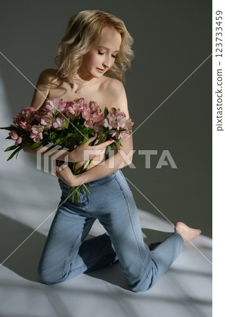 Model holding pink flowers while posing gracefully indoors Model holding pink flowers while posing gracefully indoors 123733459