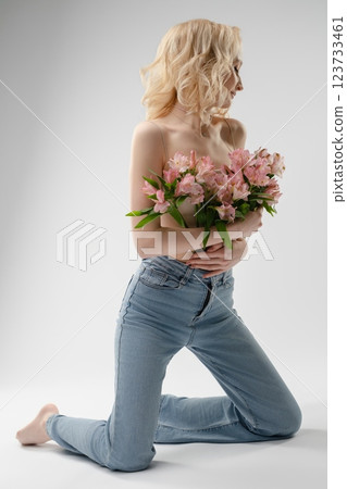 Woman in jeans kneels gracefully while holding a bouquet of pink flowers Woman in jeans kneels gracefully while holding a bouquet of pink flowers 123733461