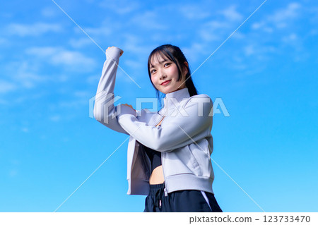 A cool woman pumping her fist in the blue sky while walking Workout Trimming 123733470