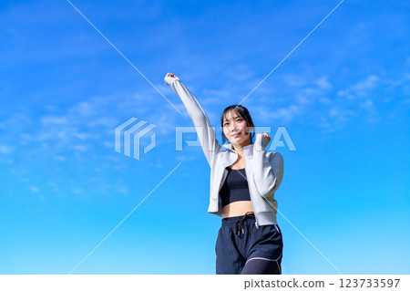 A young woman doing a cute fist pump towards the blue sky while walking Workout 123733597