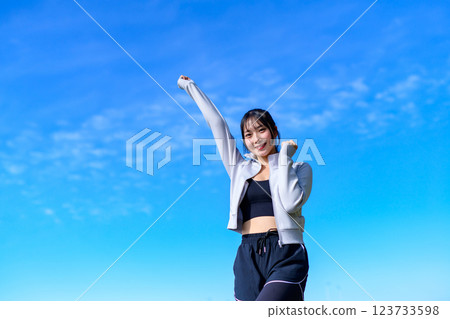 A young woman doing a cute fist pump towards the blue sky while walking Workout 123733598