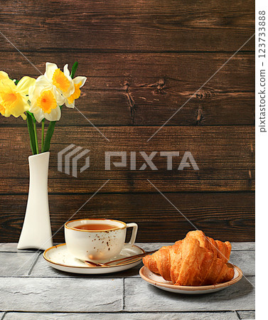 Delicious croissants, a cup of cappuccino and daffodils in a vase on a wooden table. Healthy breakfast with ingredients, the concept of a perfect morning and traditional national cuisine, bakery 123733888