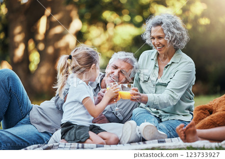 Juice, vitamin c and family picnic with child and grandparents for healthy growth development, outdoor wellness lifestyle. Senior grandmother, elderly people and girl with orange drink in bokeh park 123733927