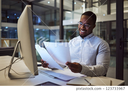 Documents, night and computer with a businessman working at his desk late in the office. Paperwork, finance and tax with a male employee at work for overtime on a deadline while reading a report 123733967