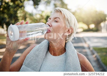 Senior fitness woman drinking water bottle outdoors after training, running workout and exercise in neighborhood street. Thirsty elderly lady runner hydration rest for cardio wellness or marathon jog 123734212
