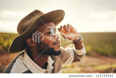 Sustainability, farm and agriculture with a black man or cowboy farmer chewing straw in a grass field or meadow. Sustainable, farming and sustainable with a young male working in organic ecology 123734591