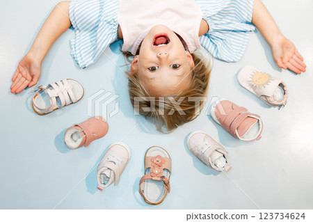 Child, shoes and head above floor with smile on face against blue backdrop. Girl, happy and sandal in mockup excited with happiness, color and summer fashion against studio background in Sweden 123734624
