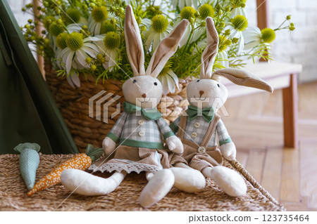 Decorative toy bunnies with carrots on wicker surface on flower bouquet background 123735464