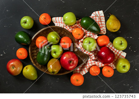Apples, pears, oranges and avocado in wooden carved bowl on black marble like board, view from above 123735743