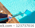 Close-up of skimmer net cleaning turquoise water in swimming pool with wooden deck 123737016