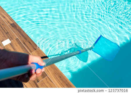 Close-up of skimmer net cleaning turquoise water in swimming pool with wooden deck 123737016