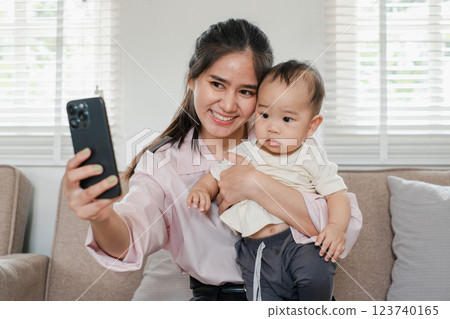 Smiling mother holding her baby while taking a selfie in a bright and cozy living room setting. 123740165