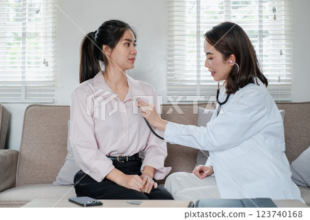 Female doctor using a stethoscope to examine a patient in a cozy living room environment, highlighting home healthcare. Female doctor using a stethoscope to examine a patient in a cozy living room environment, highlighting home healthcare. 123740168