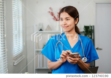 Smiling healthcare professional in blue scrubs using a smartphone in a bright, modern medical office environment. Smiling healthcare professional in blue scrubs using a smartphone in a bright, modern medical office environment. 123740190