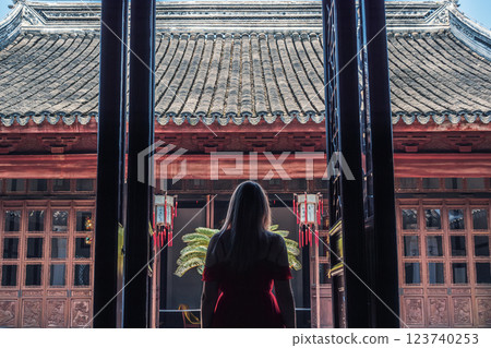 A woman stands in a doorway, gazing at the intricate details of a traditional building, surrounded by lanterns and greenery in an ancient city. A woman stands in a doorway, gazing at the intricate details of a traditional building, surrounded by lanterns and greenery in an ancient city. 123740253