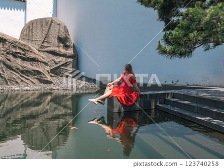 Woman in red dress relaxing by serene water in a tranquil garden in summer Woman in red dress relaxing by serene water in a tranquil garden in summer 123740258