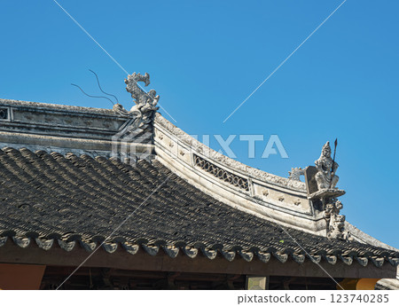 Traditional Asian architectural rooftop with intricate dragon ornamentation under clear blue sky Traditional Asian architectural rooftop with intricate dragon ornamentation under clear blue sky 123740285