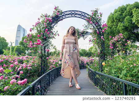Young woman in floral dress walking through rose garden during golden hour Young woman in floral dress walking through rose garden during golden hour 123740291