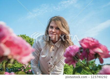 Young woman in a garden poses amidst blooming roses on a sunny day with blue sky in the background Young woman in a garden poses amidst blooming roses on a sunny day with blue sky in the background 123740292