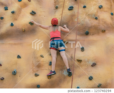 Young climber ascends a rock wall during a summer day at an outdoor adventure park in a vibrant setting Young climber ascends a rock wall during a summer day at an outdoor adventure park in a vibrant setting 123740294