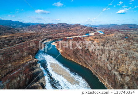 Winding river flows through a scenic valley with bare trees and mountains in the backdrop during early spring. The 123740354