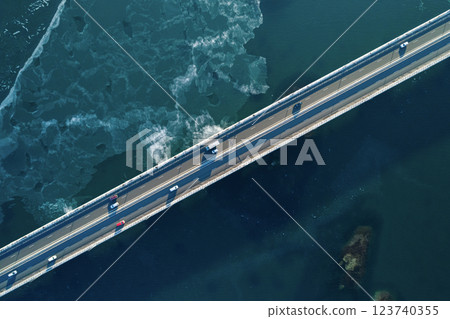 Aerial top down view of a cars driving along a coastal bridge with clear waters and ocean waves beneath in bright daylight 123740355