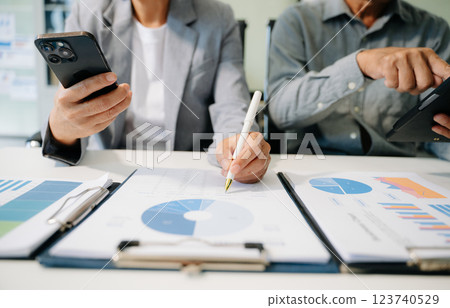 Business documents on office table with smart phone and laptop and two colleagues discussing data Business documents on office table with smart phone and laptop and two colleagues discussing data 123740529