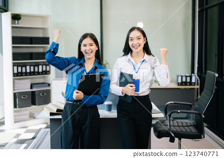 Professional women smiling confidently, collaborating with a tablet and clipboard in a modern office. 123740771