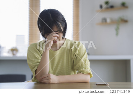 A woman in her 30s holding her head at the table at home A woman in her 30s holding her head at the table at home 123741349