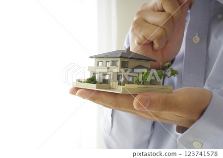 A man thinking with a model house in his hands 123741578