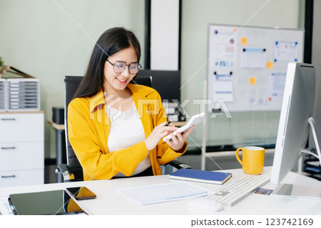 Young Asian businesswoman working with working notepad, tablet and laptop documents talking Young Asian businesswoman working with working notepad, tablet and laptop documents talking 123742169