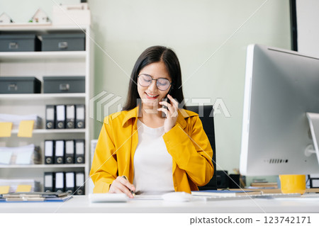 Young Asian businesswoman working with working notepad, tablet and laptop documents talking 123742171