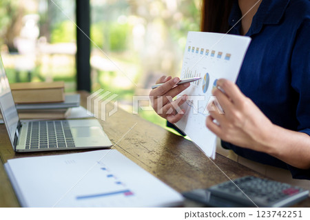 Businesswoman in a natural-themed office conducting a virtual meeting on a laptop, presenting documents professionally. 123742251