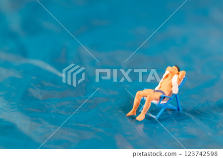 A man lounges on a beach chair, enjoying a peaceful moment on a textured blue surface resembling water 123742598