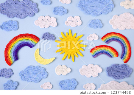 Knitted toys blue and white clouds, yellow sun, rainbow, moon on blue background. Baby stuff and accessories. Top view, flat lay, banner 123744498