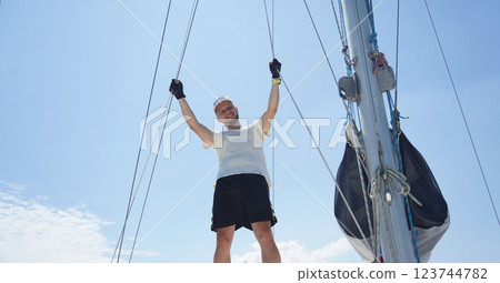 Male captain on deck of sailboat opening sails pulling the rope 123744782