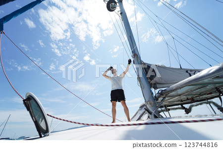 Male captain on deck of sailboat opening sails pulling the rope Male captain on deck of sailboat opening sails pulling the rope 123744816