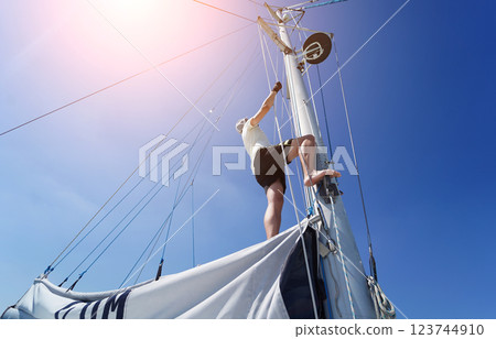 Male captain climbing mast of sailboat to check sails 123744910
