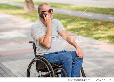Handicapped man in wheelchair at the park alley use a smartphone Handicapped man in wheelchair at the park alley use a smartphone 123745006