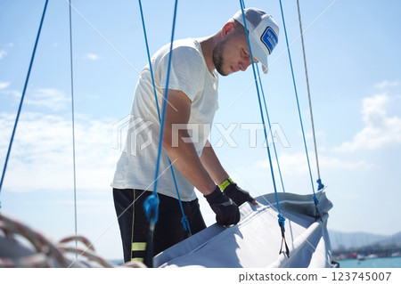 Male captain on deck of sailboat unpacking sails pulling zipper 123745007