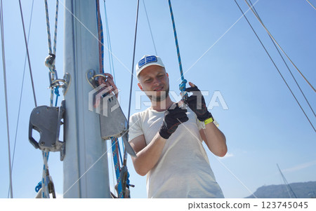 Male captain on deck of sailboat opening sails pulling the rope 123745045